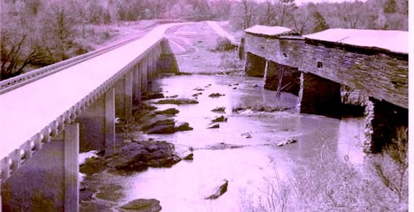 Black and white photo of a newly constructed bridge paralleling and older covered wooden bridge spanning a river.