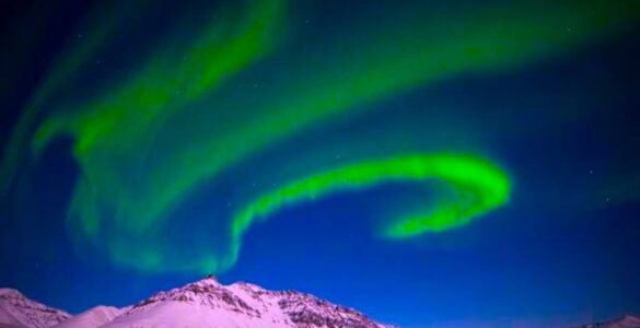 Florescent green aurora bands in a dark blue sky above a melting snowy polar landscape.