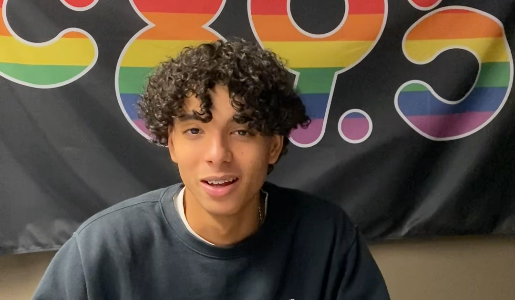 A photo of a teenage boy. He has light brown skin, brown curly hair and is smiling.