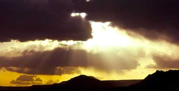 Rugged landscape bathed in the golden unseen sunset. Dark, rolling hills stretch towards a horizon ablaze with yellow.