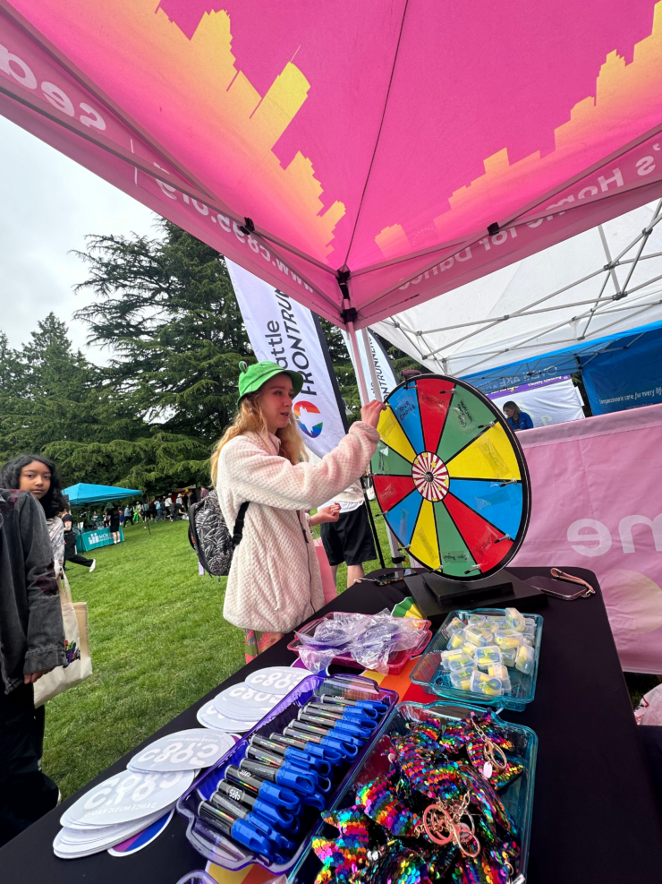 Person spinning a prize wheel at an outdoor event booth with various promotional items on display, including pens and bracelets.