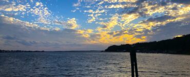 Calm lake at dusk. Blue water with a darkening shoreline. Elements of color linger in the clouds of the twilight sky.