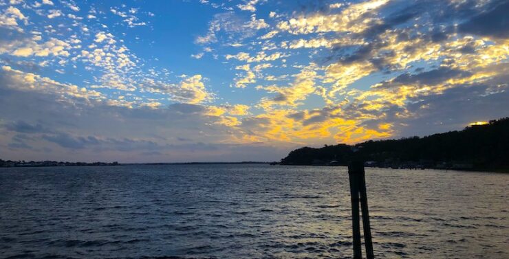 Calm lake at dusk. Blue water with a darkening shoreline. Elements of color linger in the clouds of the twilight sky.