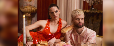 Sofi & Tukker from Sofi Tukker posing at an opulent dining table adorned with an array of pastries and fine glassware, wearing extravagant outfits.