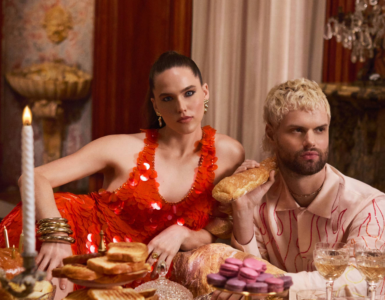 Sofi & Tukker from Sofi Tukker posing at an opulent dining table adorned with an array of pastries and fine glassware, wearing extravagant outfits.