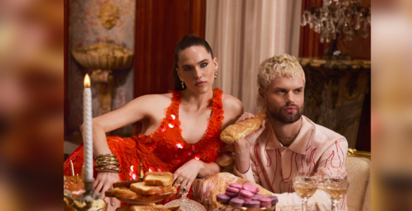 Sofi & Tukker from Sofi Tukker posing at an opulent dining table adorned with an array of pastries and fine glassware, wearing extravagant outfits.