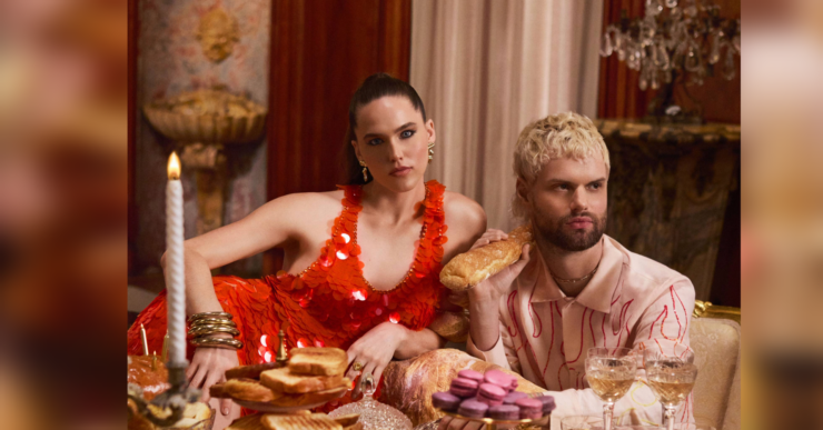 Sofi & Tukker from Sofi Tukker posing at an opulent dining table adorned with an array of pastries and fine glassware, wearing extravagant outfits.