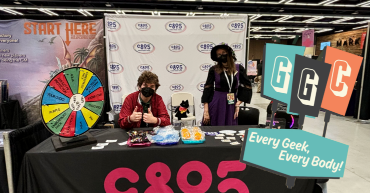 Two individuals at a CB95 promotional booth at a convention, featuring a prize wheel, merchandise, and banners. The booth is adorned with a 'Start Here' sign and the motto 'Every Geek, Every Body'.