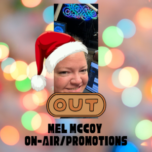 an adult female with hazel eyes smiling in front of the on-air studio equipment wearing a cartoon Santa Hat.