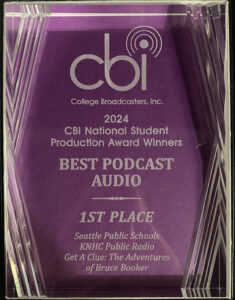 A photo of a glass trophy with the logo "cbi" and the words College Broadcasters, Inc. at the top. Below, it states: 2024 CBI National Student Production Award Winners> Best Podcast Audio. 1st Place, Seattle Public Schools, KNHC Public Radio. "Get a Clue, the Adventures of Bruce Booker."