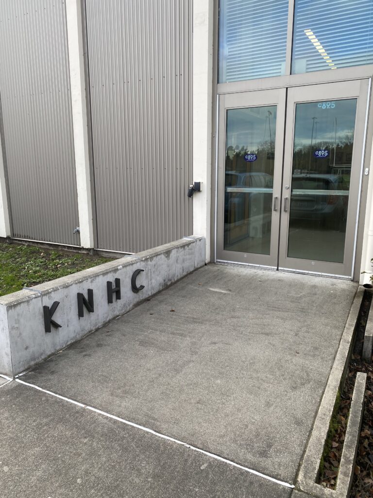  A photo of a set of glass double doors and a cement wall with the letters K N H C on the side