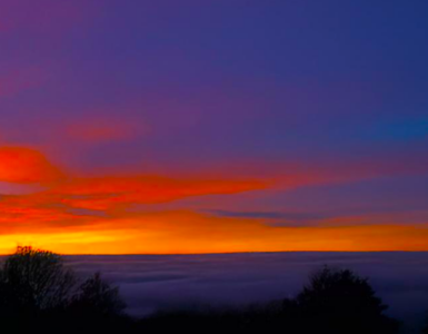 A view of a valley with clouds covering the valley floor, shortly after sunset. The sky is blue with shades of orange and red.