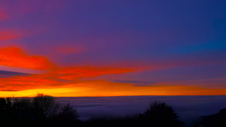 A view of a valley with clouds covering the valley floor, shortly after sunset. The sky is blue with shades of orange and red.