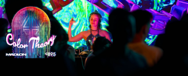 A DJ performs at a nightclub, surrounded by colorful lighting and an engaged crowd, enhancing the lively atmosphere.