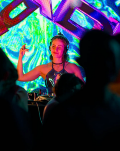 A DJ performs at a nightclub, surrounded by colorful lighting and an engaged crowd, enhancing the lively atmosphere.