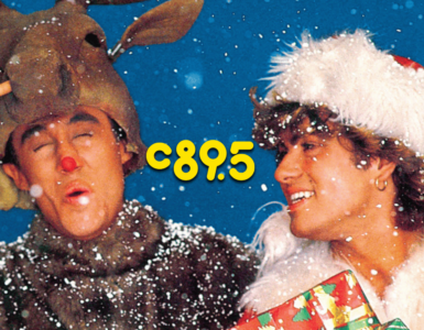 Promotional image from the song 'Last Christmas' by Wham! featuring a person in a reindeer costume winking and making a peace sign, and another person in a white fur hat smiling while holding a stack of gifts, both surrounded by falling snow.