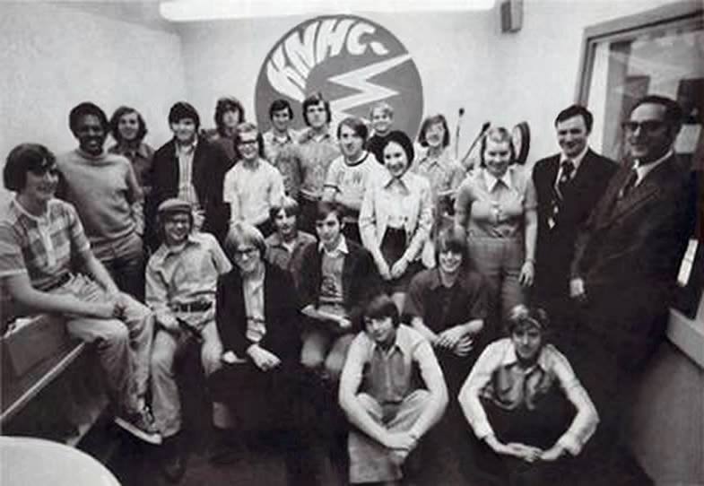 Group of people posing in a room with a large KNHC logo on the wall behind them.