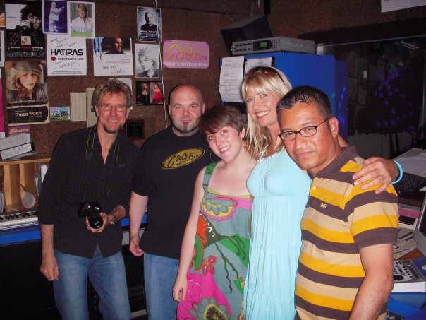 Group of five smiling adults posing in a room with posters and a microphone in the background.