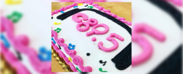 A birthday cake with pink and black frosting spelling out "c895", surrounded by colorful decorative elements.