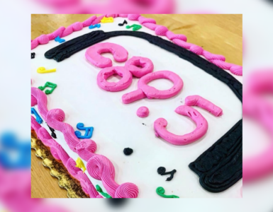 A birthday cake with pink and black frosting spelling out "c895", surrounded by colorful decorative elements.