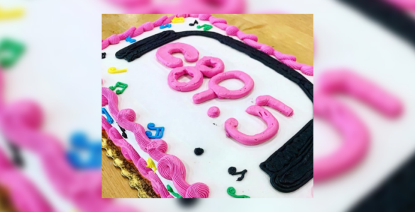 A birthday cake with pink and black frosting spelling out "c895", surrounded by colorful decorative elements.