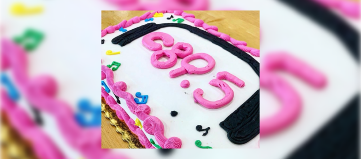 A birthday cake with pink and black frosting spelling out "c895", surrounded by colorful decorative elements.