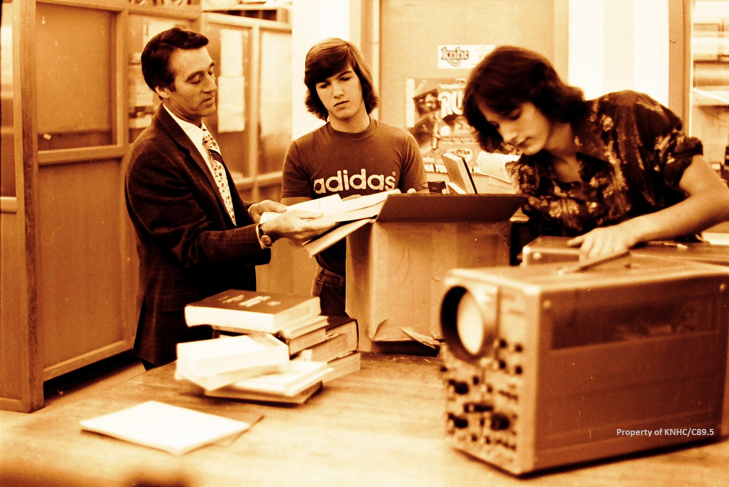 Three men standing around old equipment in a black and white photo.