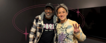 Two individuals posing for a photo in a room, one wearing a Disney-themed sweater and the other sporting a shirt with "895" printed on it.