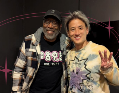 Two individuals posing for a photo in a room, one wearing a Disney-themed sweater and the other sporting a shirt with "895" printed on it.