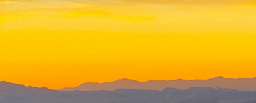 A vibrant amber sunset with the sky almost entirely in shades of amber, while the mountains below are painted in purple hues.