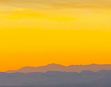 A vibrant amber sunset with the sky almost entirely in shades of amber, while the mountains below are painted in purple hues.