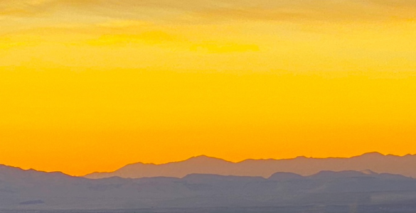 A vibrant amber sunset with the sky almost entirely in shades of amber, while the mountains below are painted in purple hues.