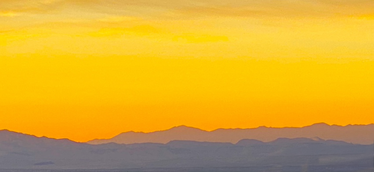 A vibrant amber sunset with the sky almost entirely in shades of amber, while the mountains below are painted in purple hues.