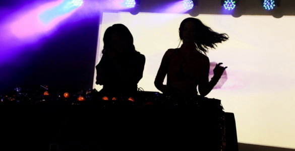 Silhouettes of two DJs performing at a music event with colorful stage lighting.