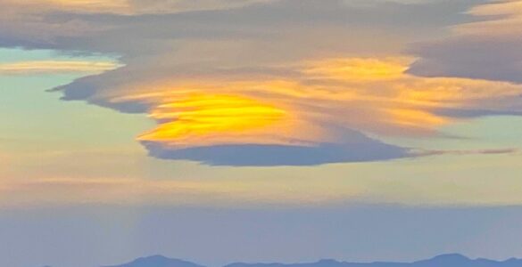 A lenticular cloud shaped like a saucer, with orange and blue hues. The mountains below are faintly visible in the fading light of dusk.